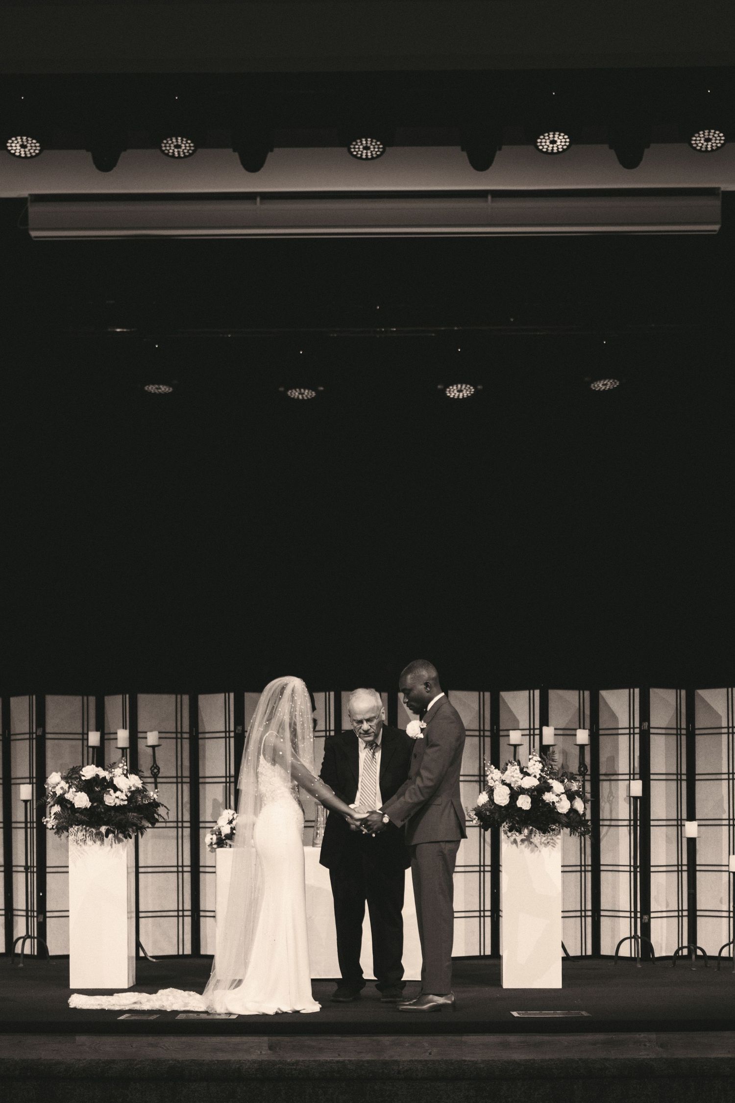 Black and white photo of a bride and groom exchanging vows with an officiant at a church altar.