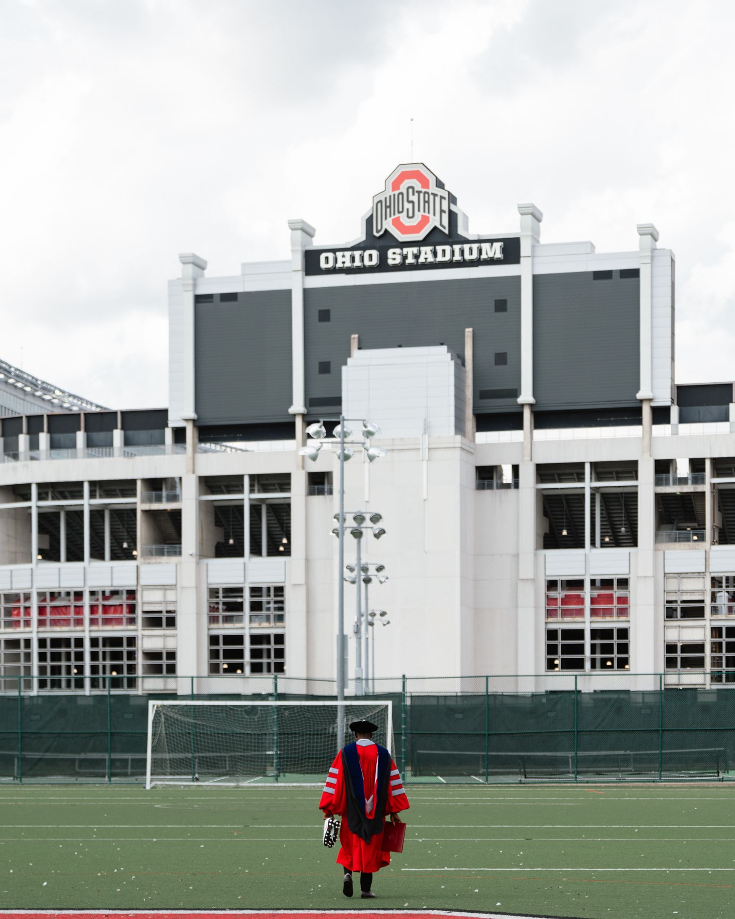 Ohio State University doctoral graduate in red regalia standing before Ohio Stadium.