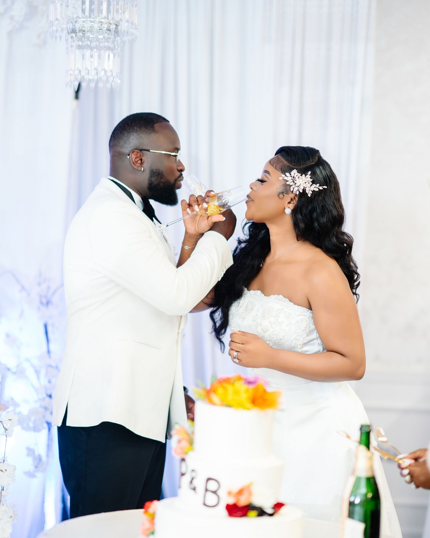 Bride and groom sharing a champagne toast near their wedding cake during elegant indoor reception.