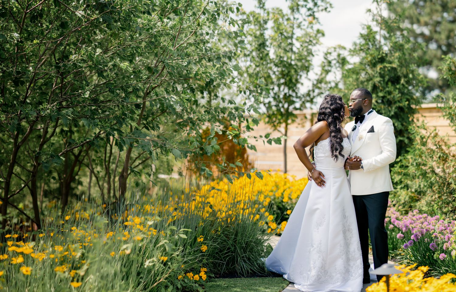 Bride and groom embracing romantically in a vibrant garden filled with yellow and purple wildflowers.