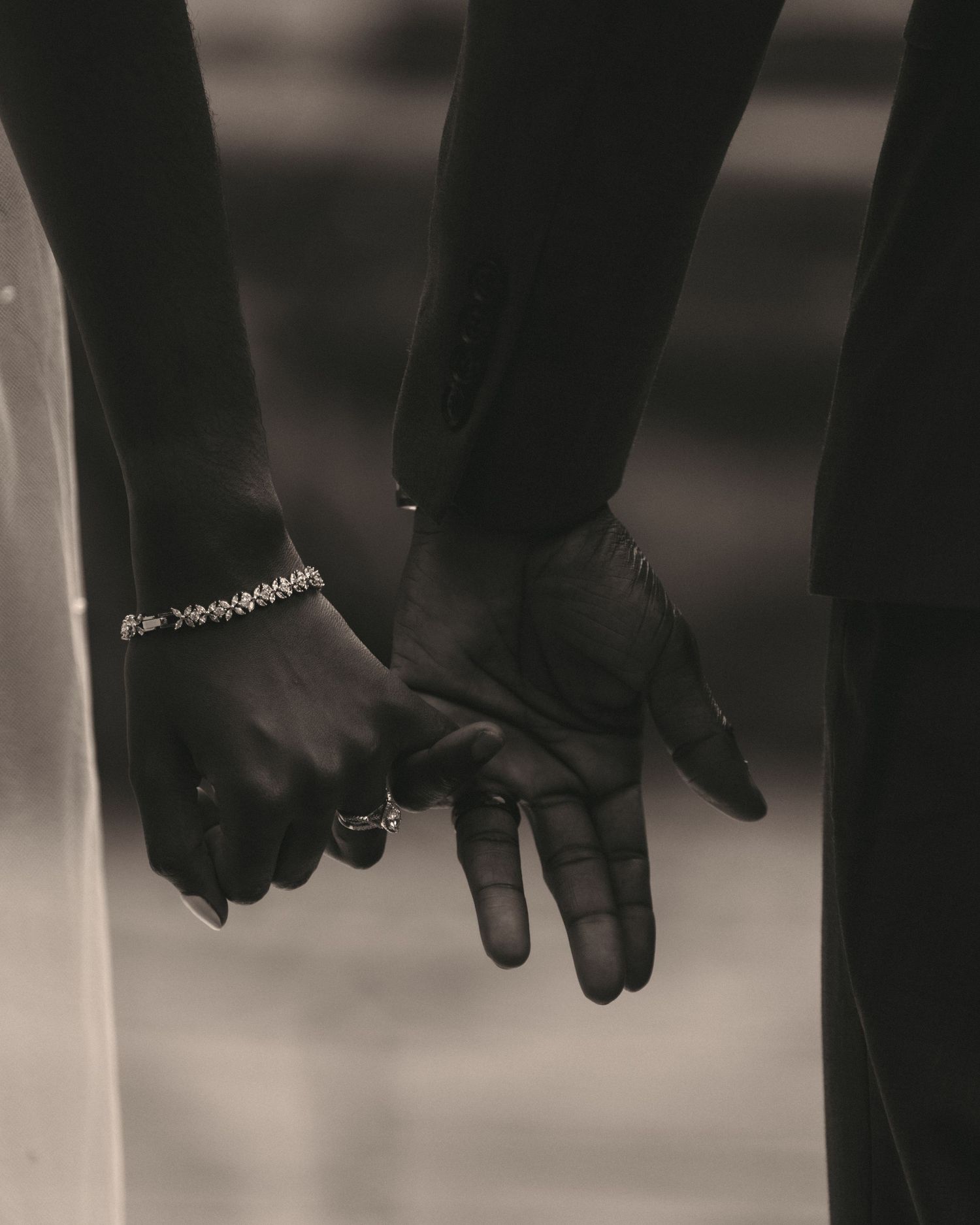 A black and white close-up of a bride and groom holding hands with a diamond bracelet.