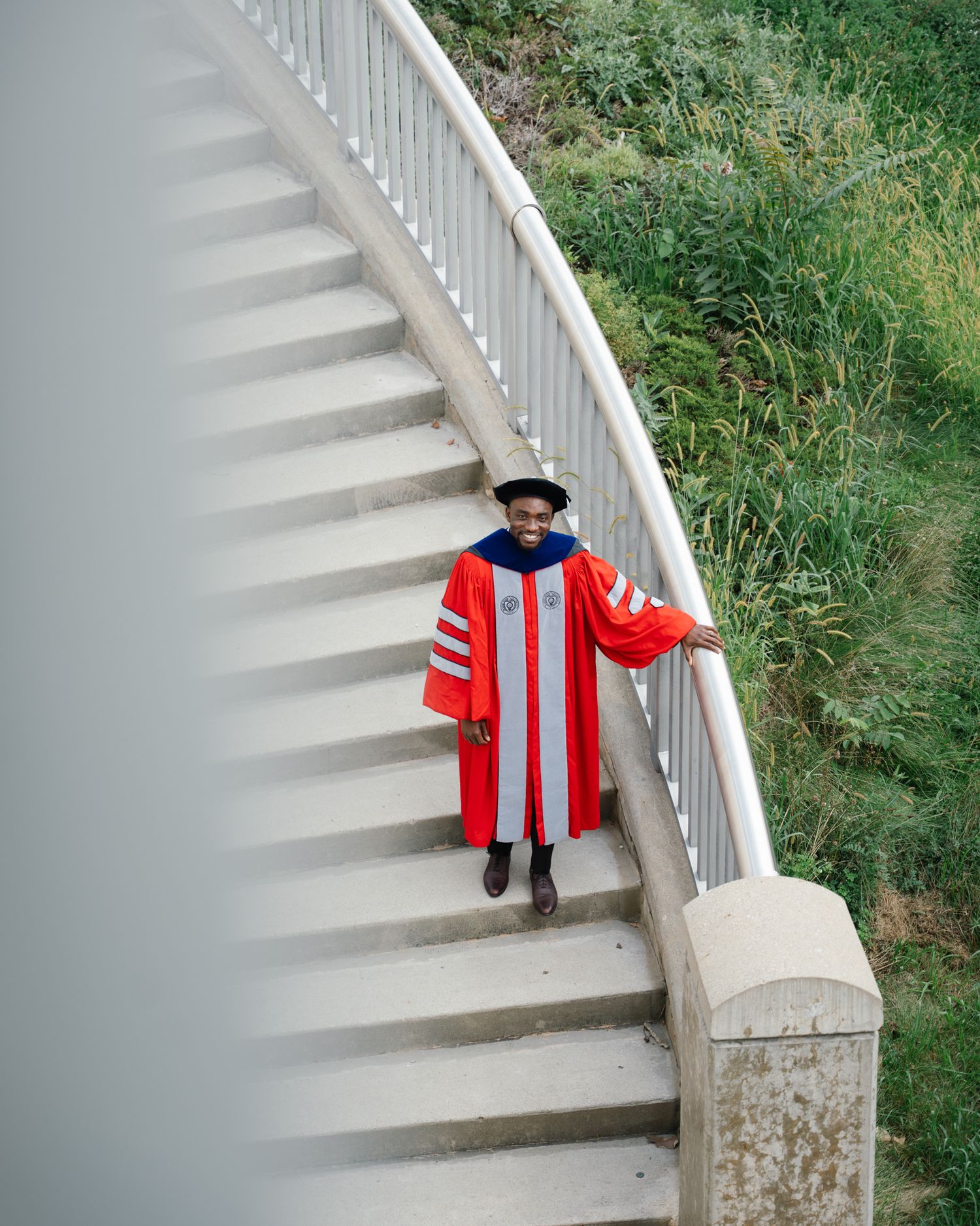 Graduate in red doctoral regalia posing on curved staircase outdoors at Ohio State University.