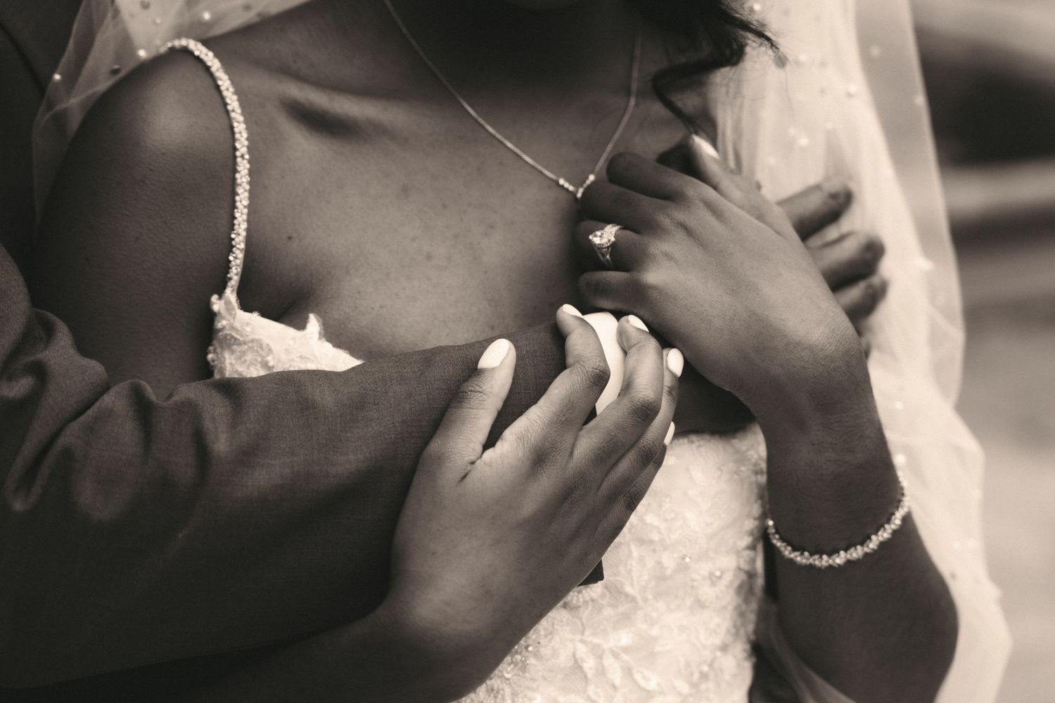 Close-up black and white photo of bride and groom hands with wedding rings and bridal jewelry.