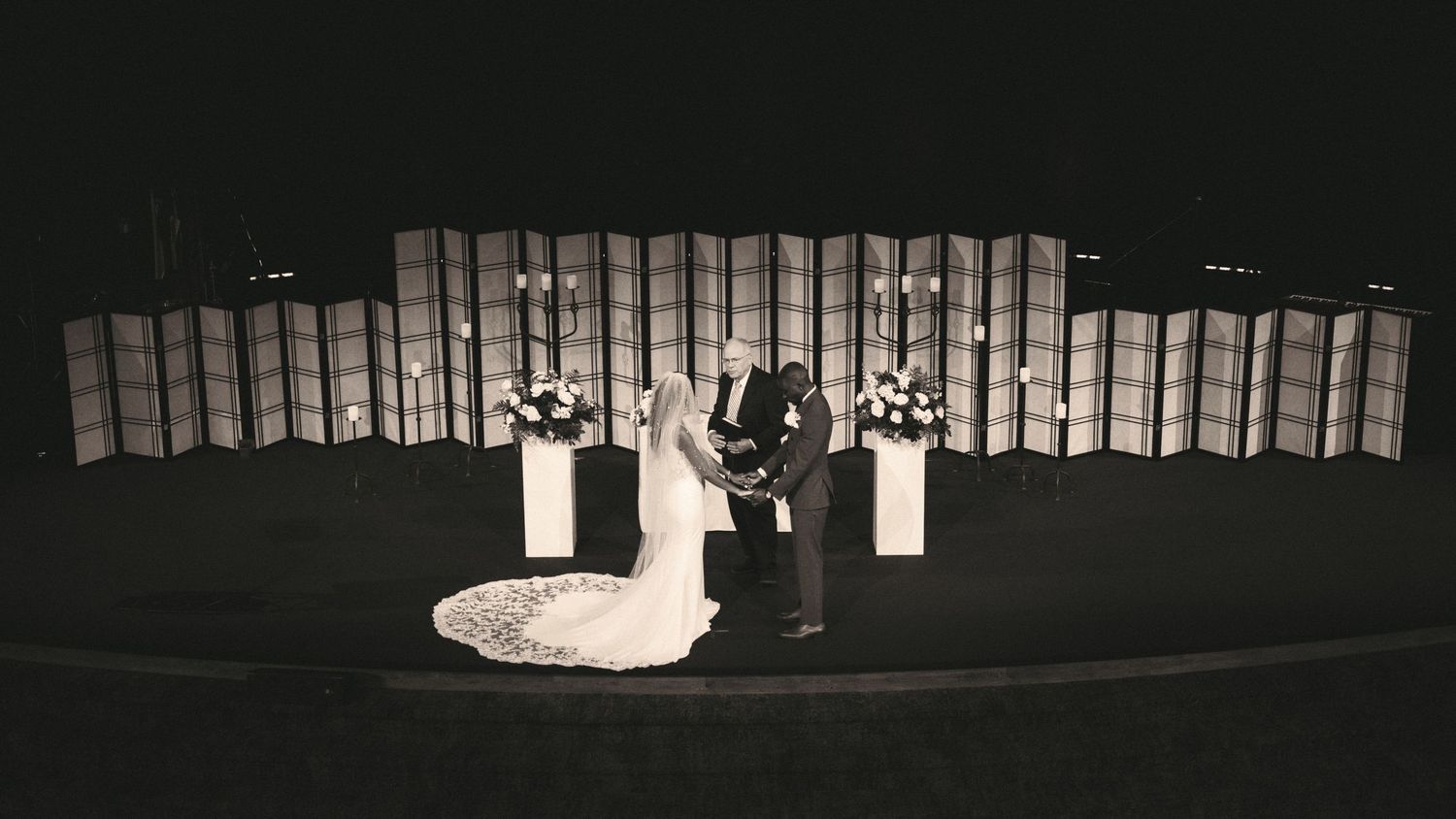 Black and white aerial view of bride and groom exchanging vows at elegant outdoor wedding ceremony.