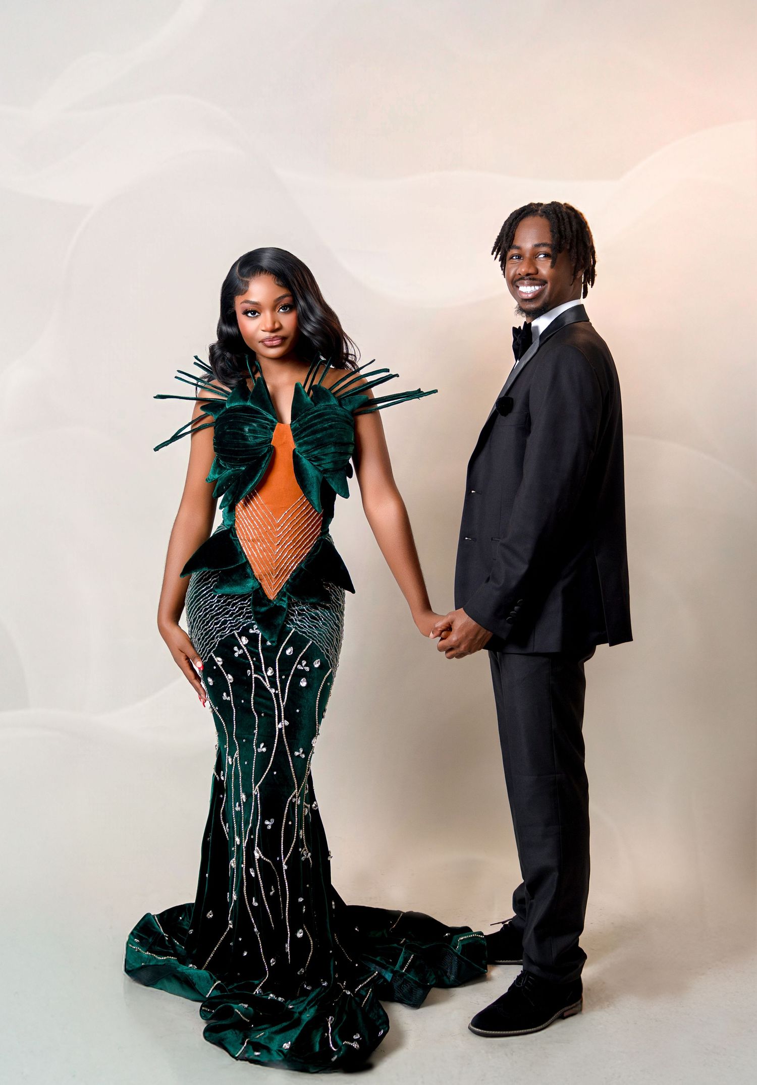 A couple posing elegantly, the woman in a stunning green and orange feathered gown and the man in a black tuxedo.