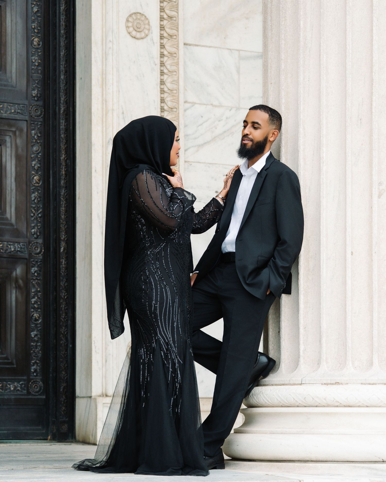 Couple in elegant black formal wear sharing a tender moment by marble columns.