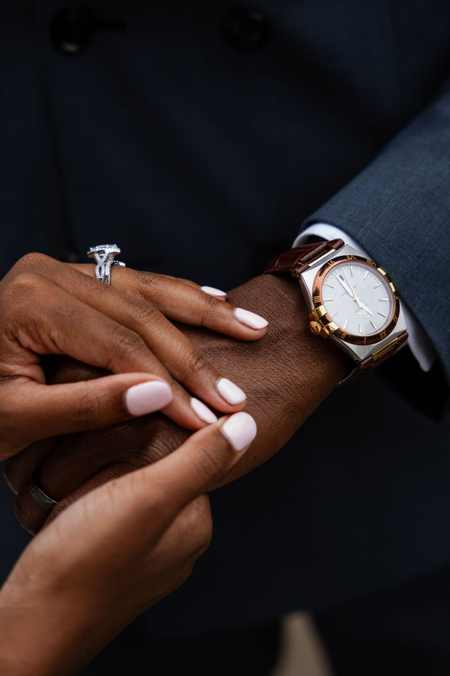Close-up of bride and groom hands, diamond engagement ring and gold watch visible on wedding day.