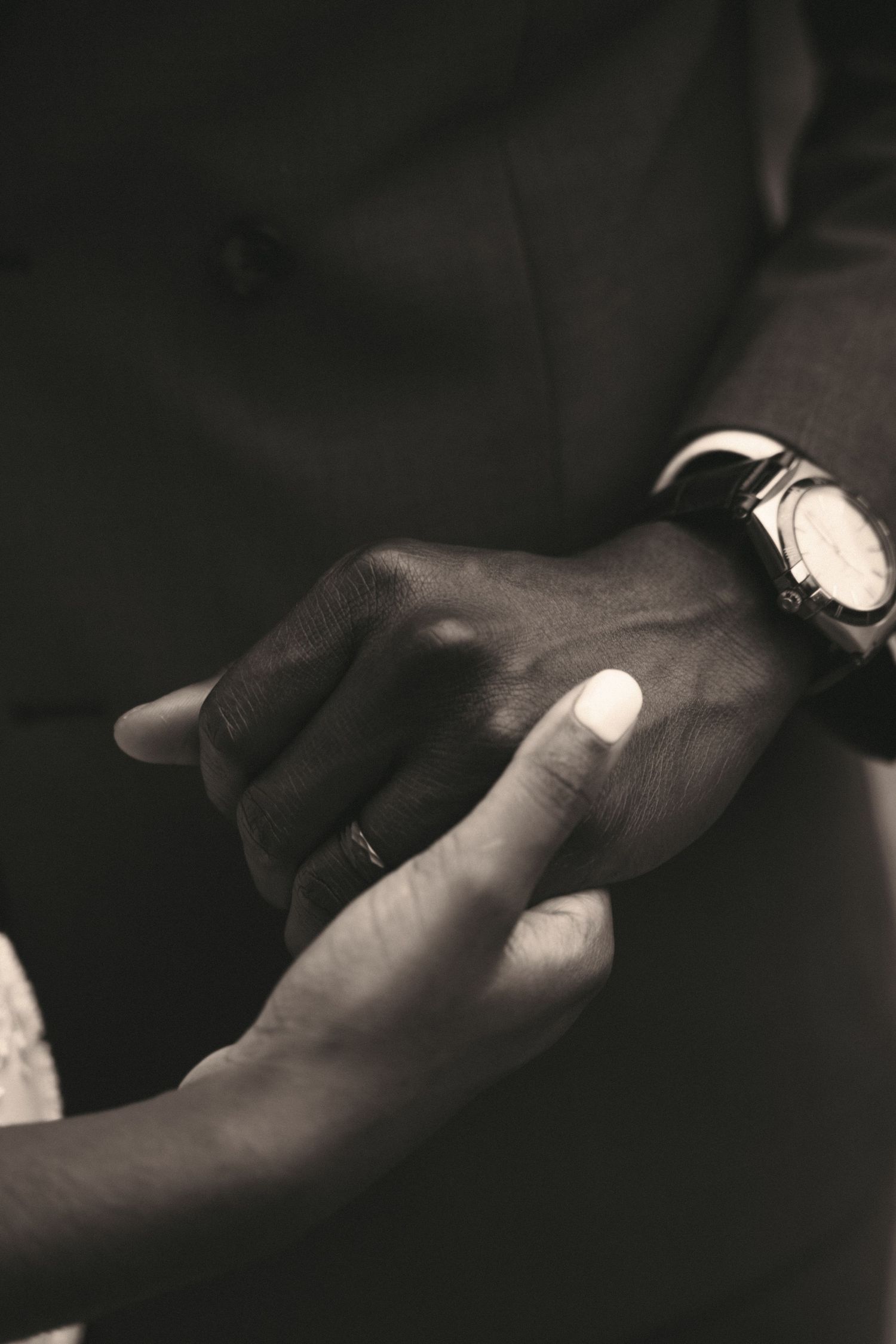 A black and white close-up of a bride and grooms hands with wedding rings and a watch.