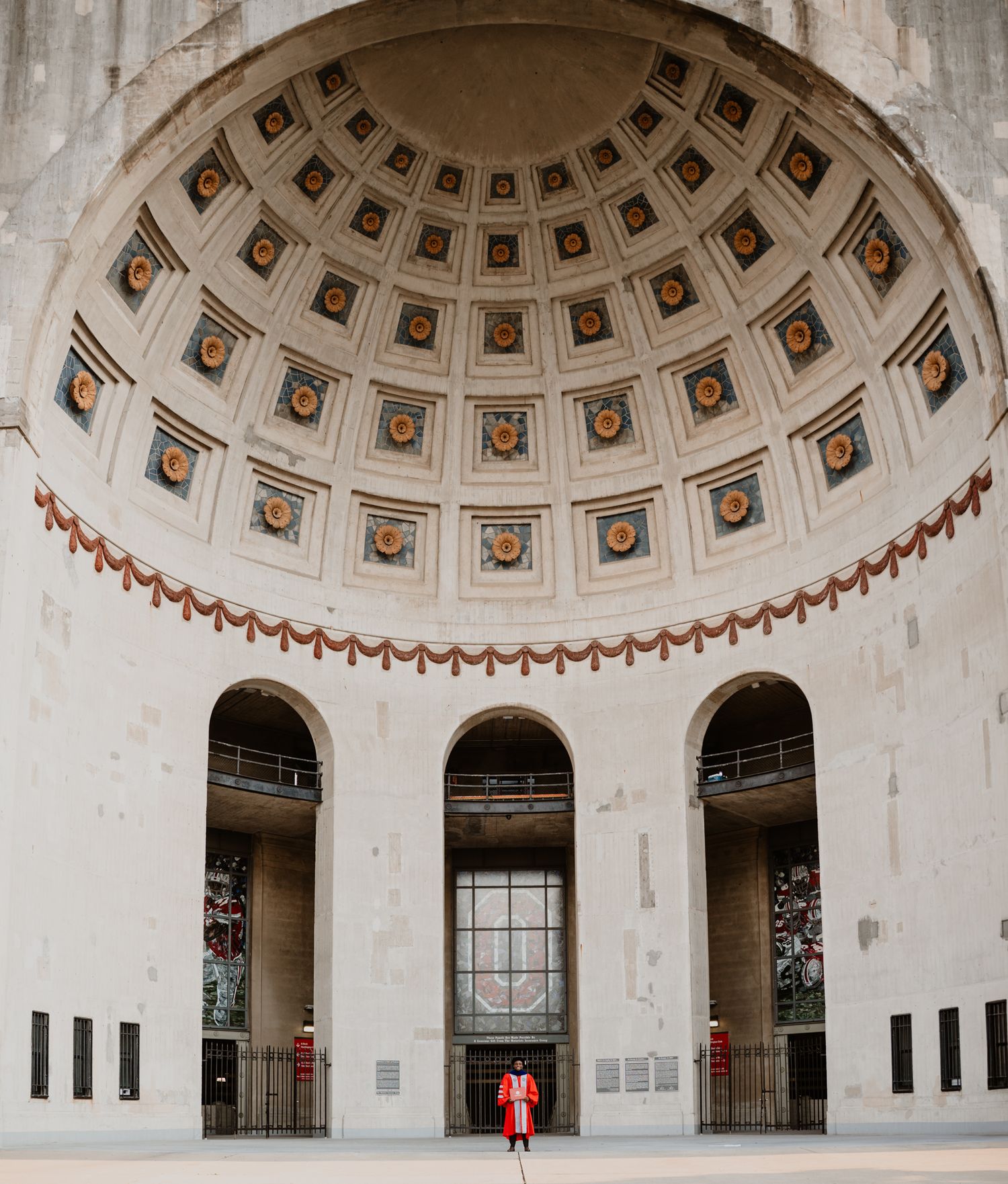 Graduate in red regalia standing beneath grand ornate domed rotunda at Ohio State University.