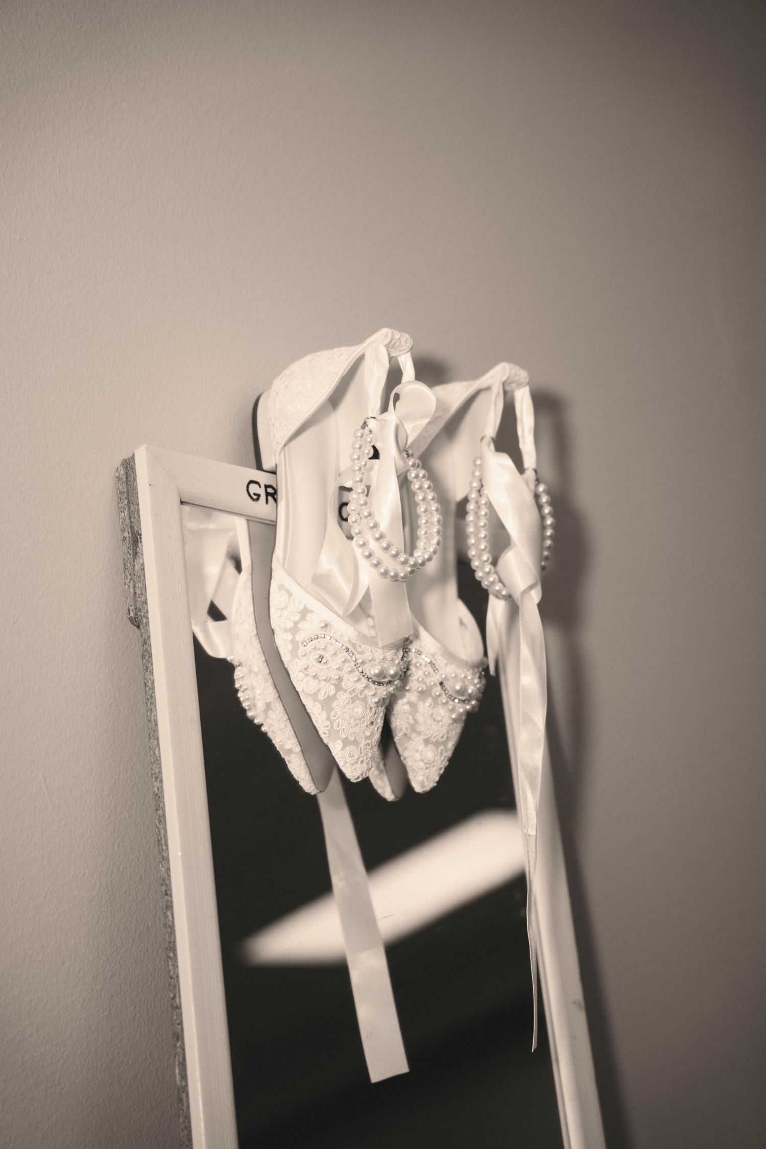 Elegant white lace bridal shoes with pearl details hanging on a decorative ladder.