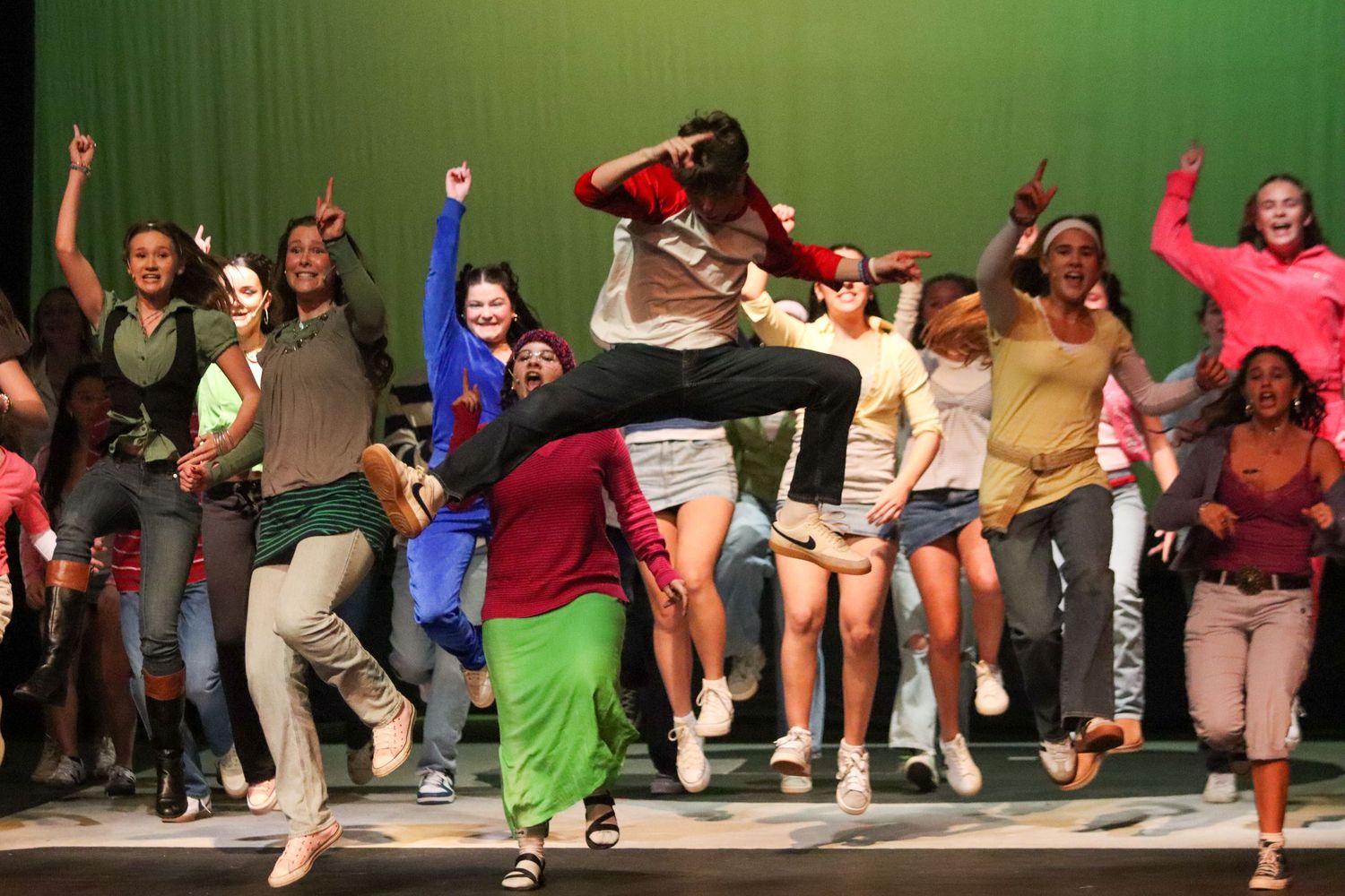 Diverse group of students jumping and dancing in colorful school musical performance.