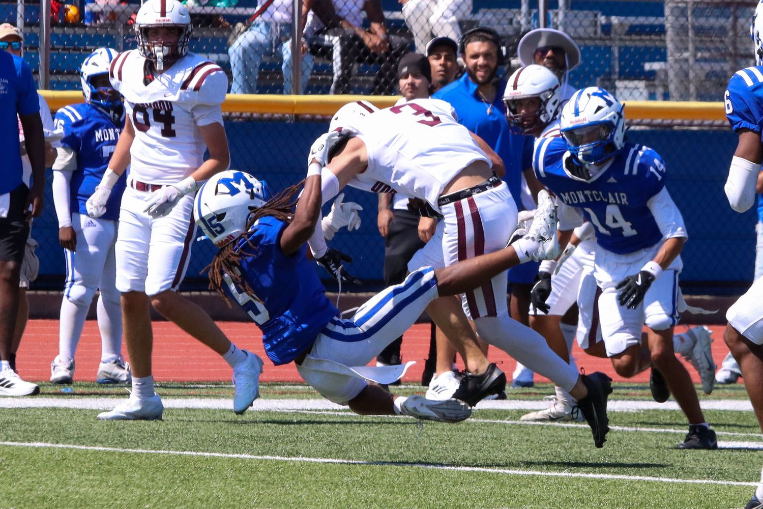 Football players tackling opponent during competitive high school game on blue turf field.