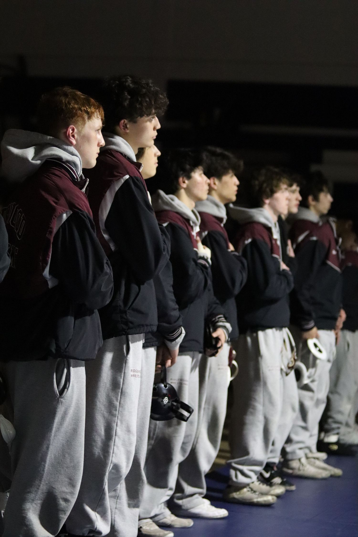 High school wrestling team members stand in a line wearing maroon and black warm-up gear.