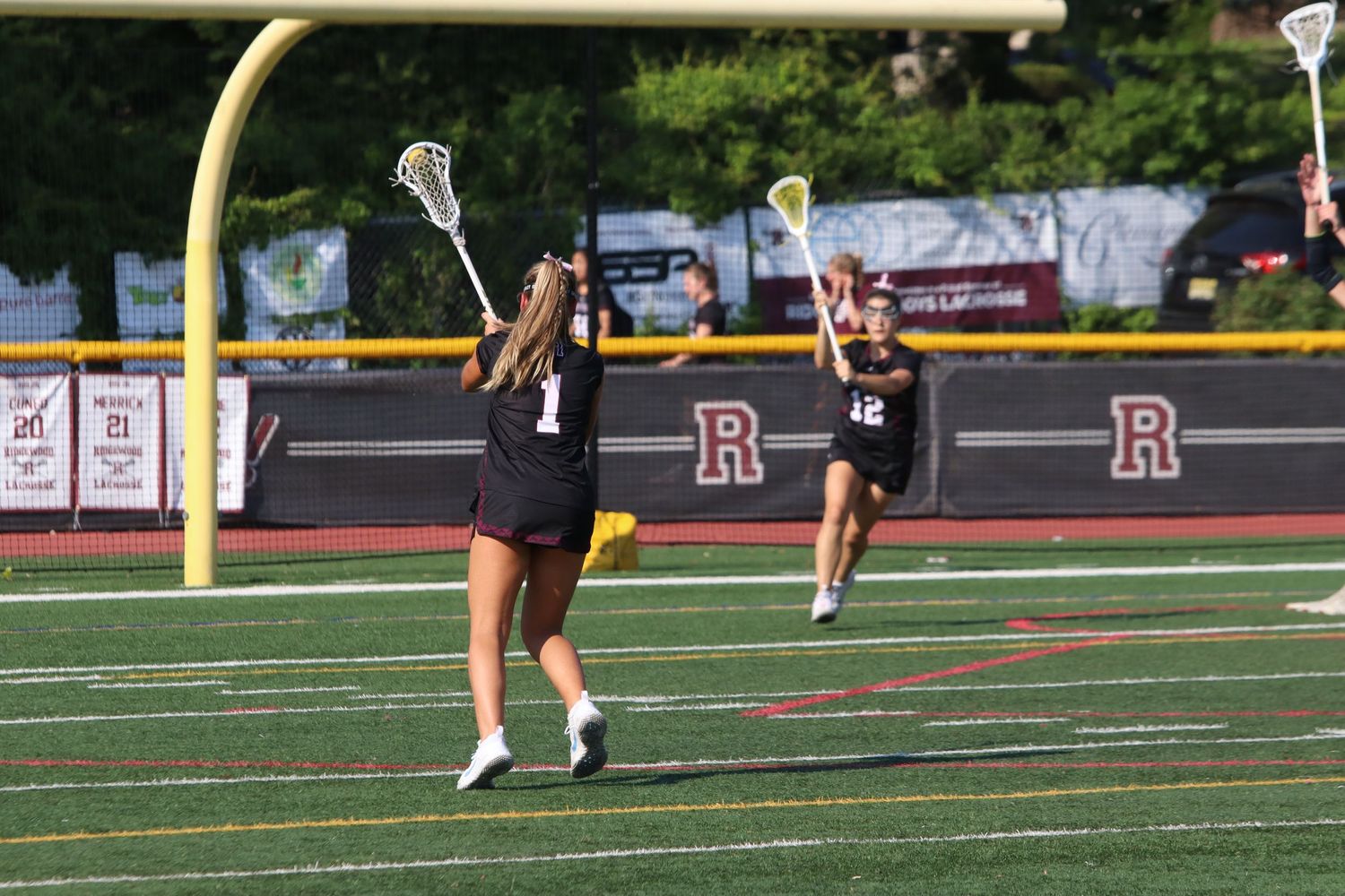 Girls lacrosse players in maroon uniforms practice passing drills on a turf field.