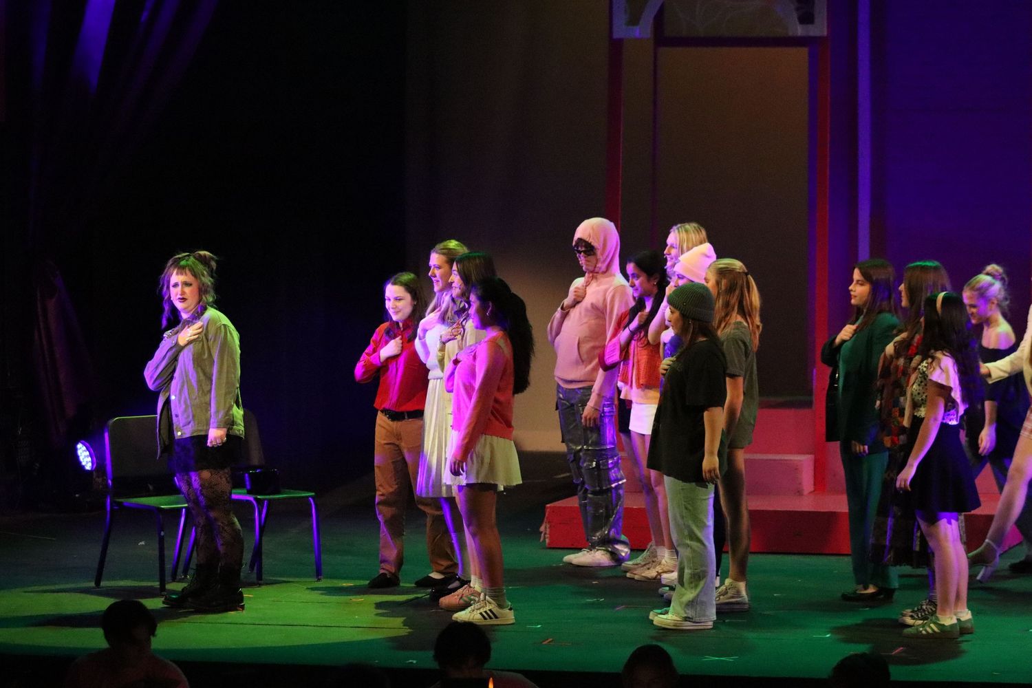 Students in casual costumes stand on stage during school theater production performance.