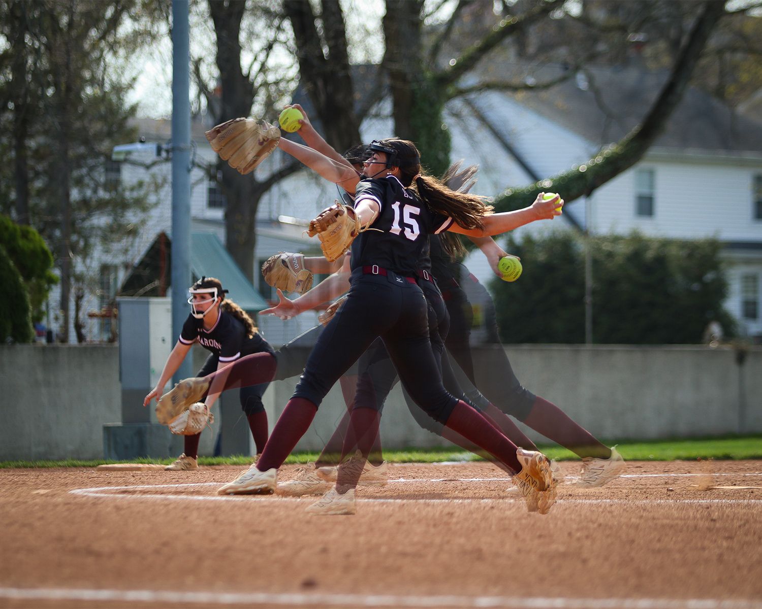 Multi-exposure softball pitcher in maroon jersey number 15 throwing ball during outdoor game.