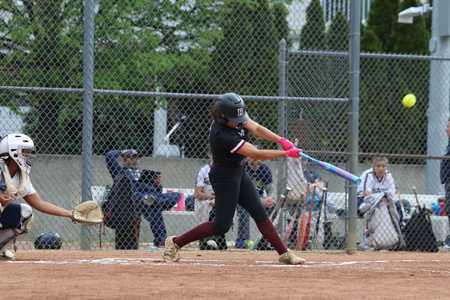 Female softball batter in maroon uniform swinging at a pitch during a game.