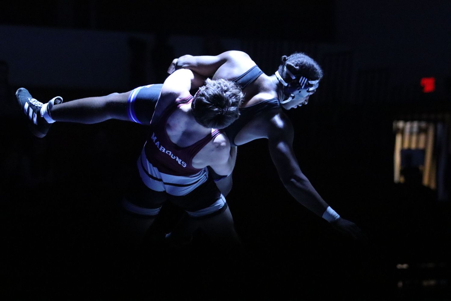 Two wrestlers compete in a dramatic grappling match under dramatic spotlight lighting.