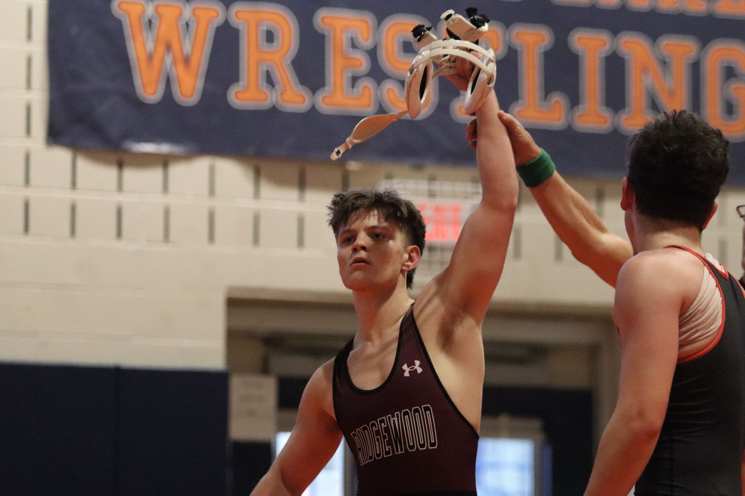 Victorious wrestler in maroon singlet has his arm raised in victory at a wrestling meet.