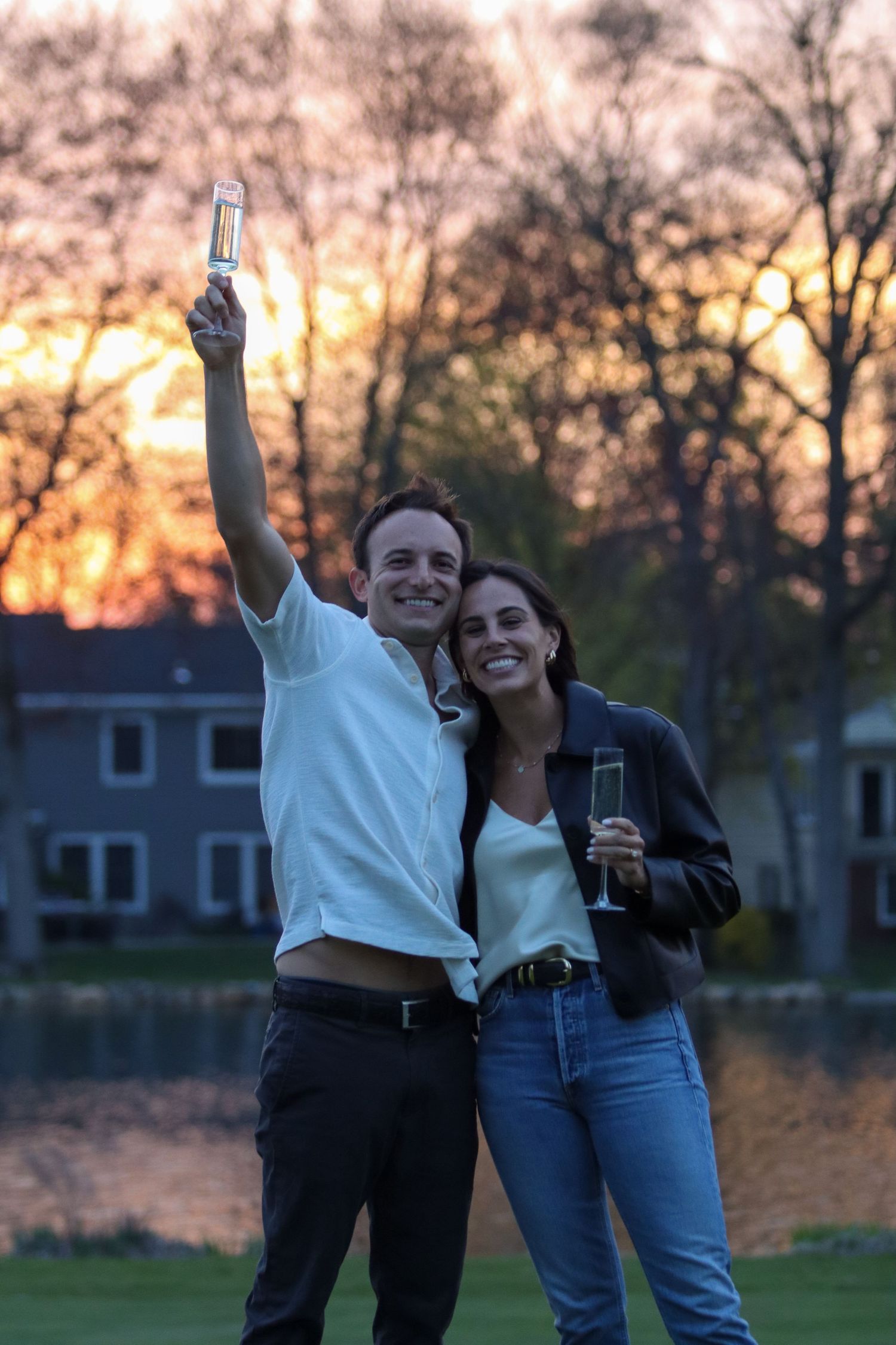 Couple celebrating at sunset toasting with champagne glasses outdoors near a lake.