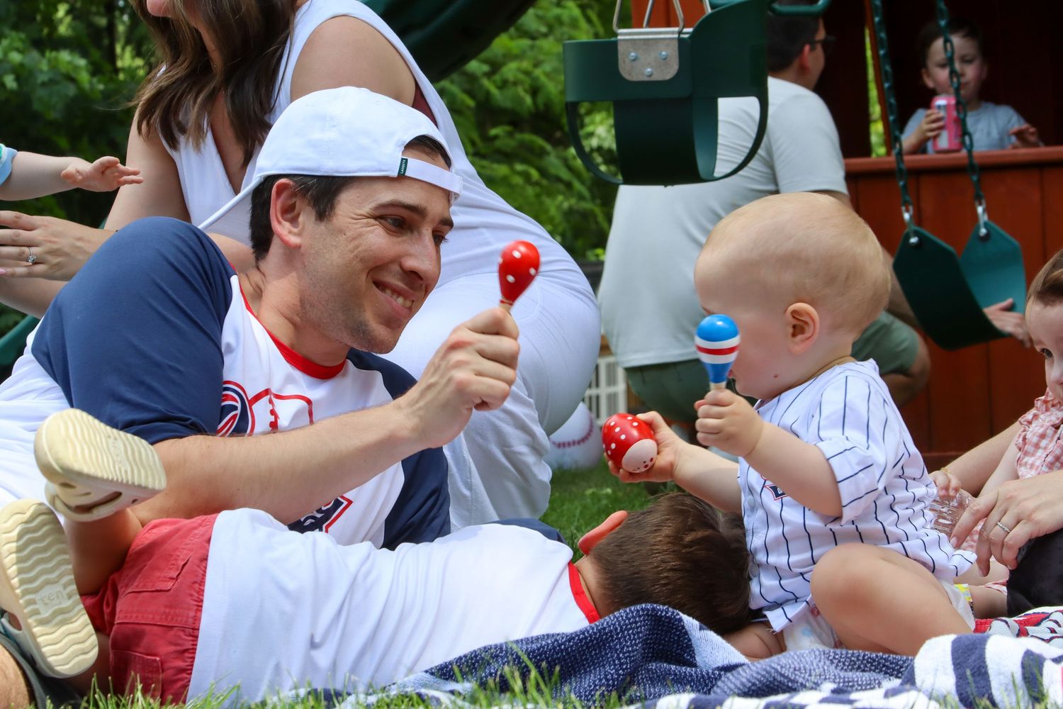 Father plays with maracas entertaining smiling baby at an outdoor summer picnic.