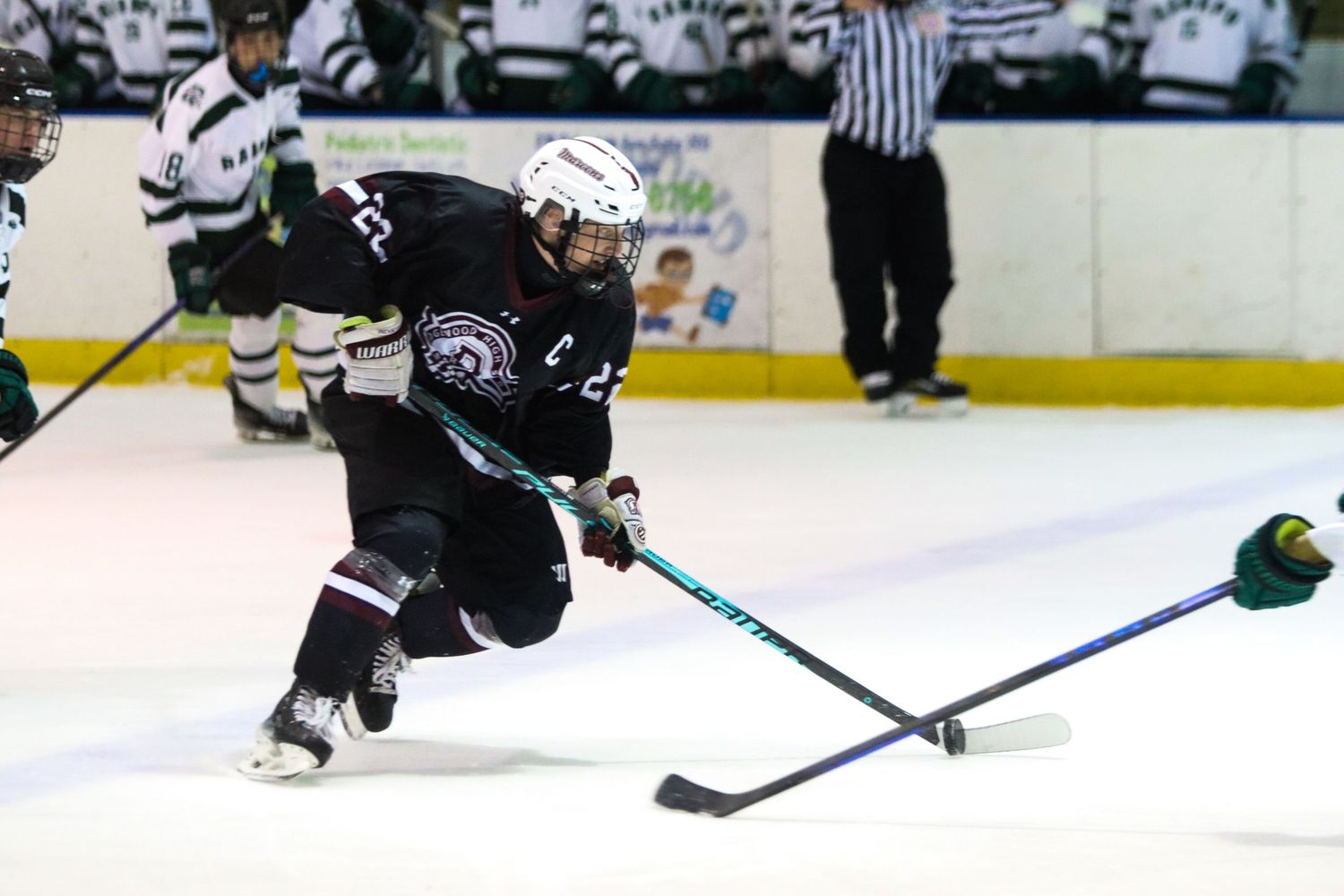 Hockey player in black uniform takes a powerful shot on ice during a competitive game.