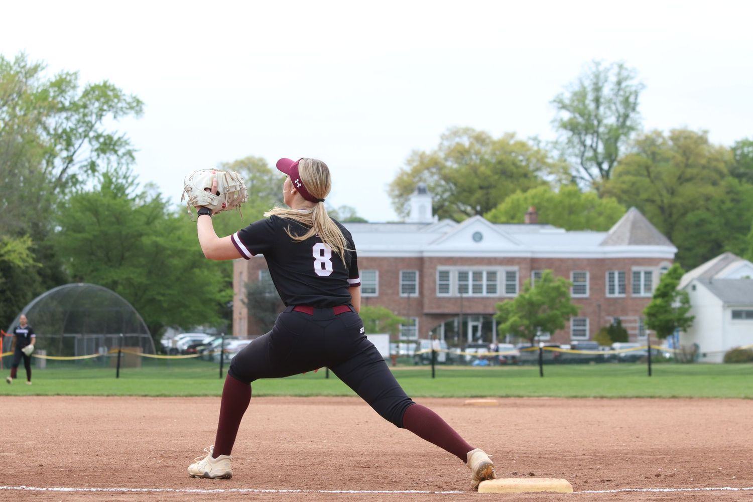 Female softball player in maroon uniform catching ball during outdoor game.