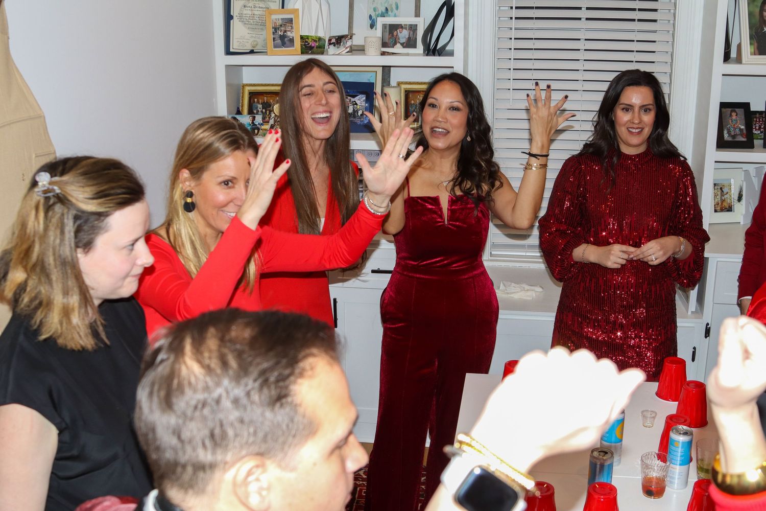 Group of women in red dresses celebrating with raised hands at a festive party.