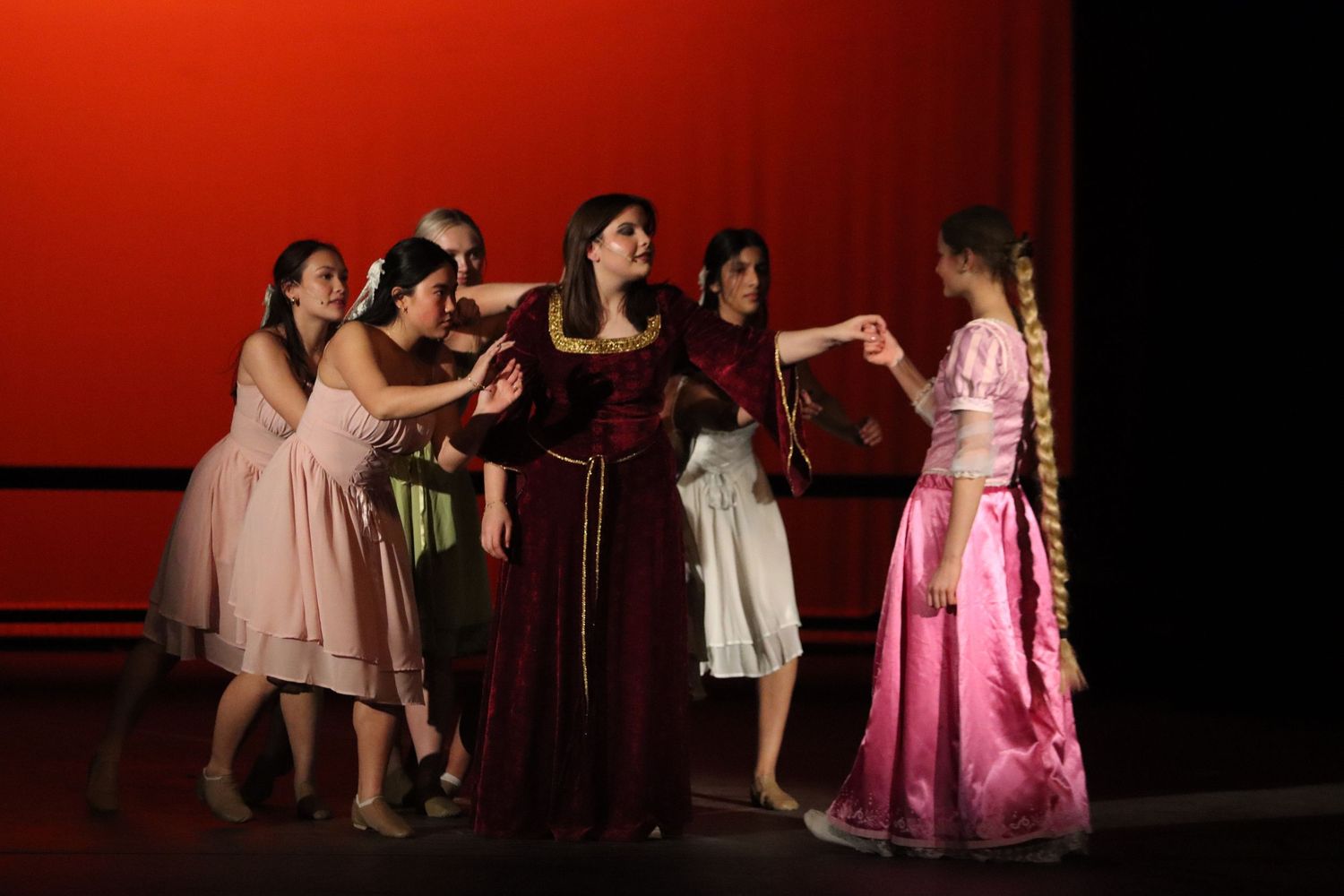 Young actresses in period costumes perform dramatic scene in school theater production.