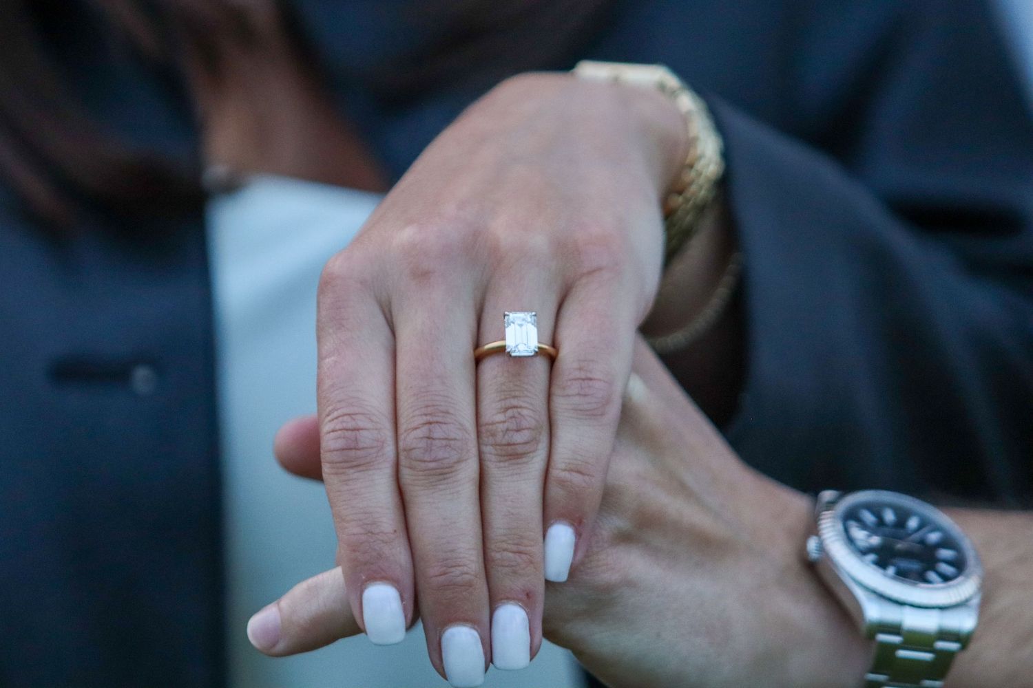 Close-up of elegant emerald cut diamond engagement ring on hand with white manicure.