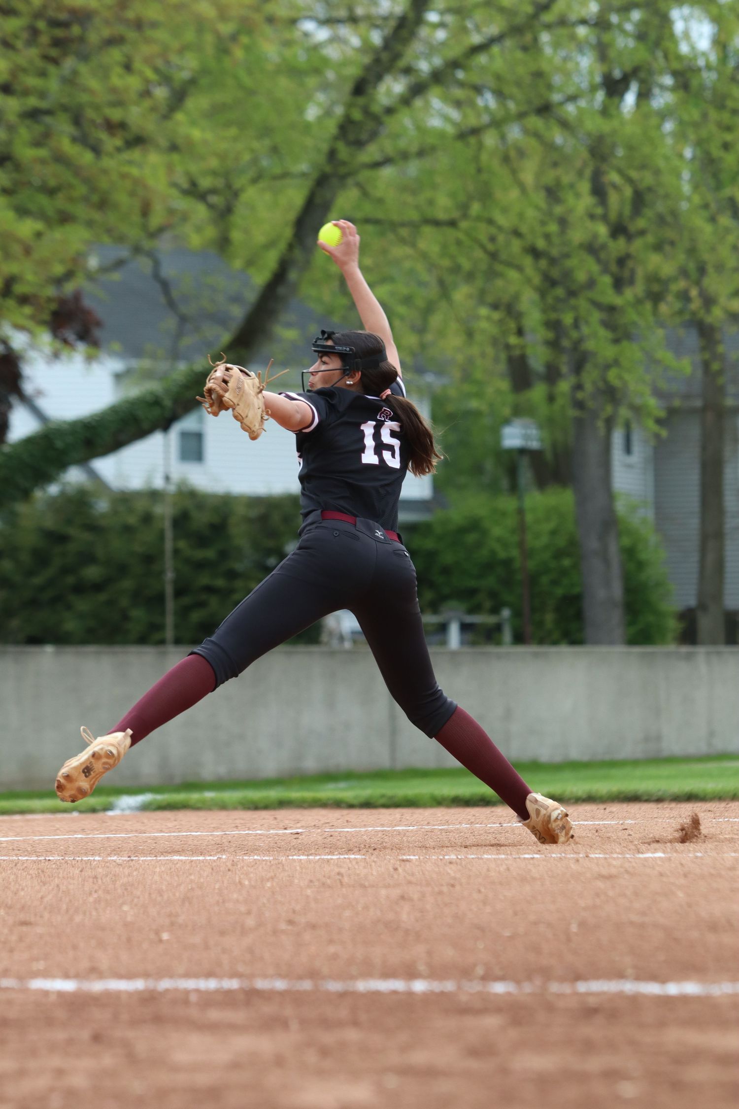 Female softball pitcher in maroon uniform delivering a windmill pitch during game.