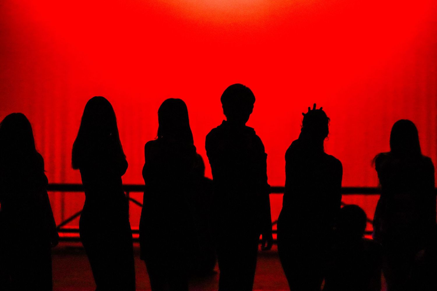 Silhouettes of performers standing dramatically against vivid red stage lighting.