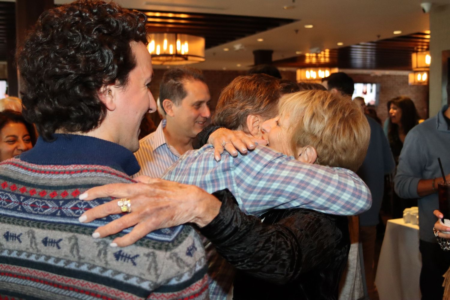 Group of people sharing warm hugs and embraces at indoor social gathering or celebration.