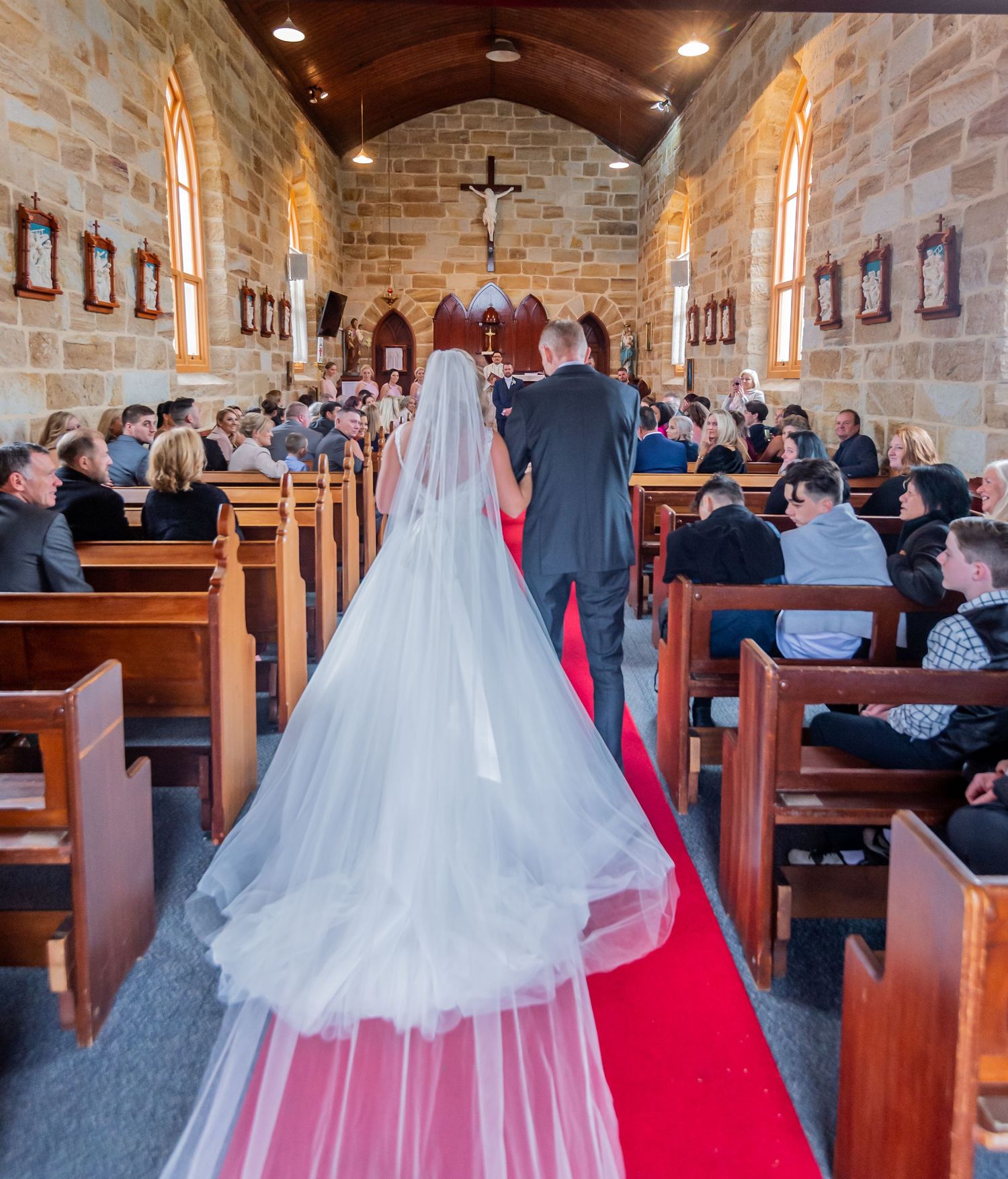 Traditional stone church interior with cathedral ceiling and red carpet aisle during wedding ceremony.