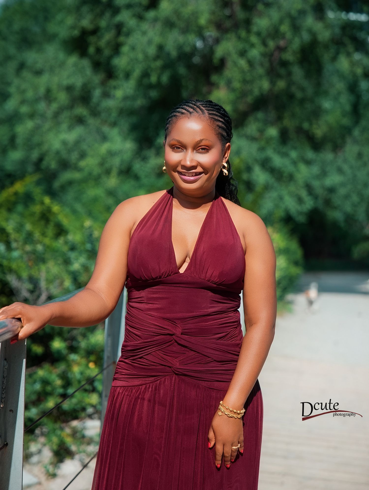 Smiling woman in burgundy halter dress posing outdoors on bridge with greenery in relaxed outdoor birthday photoshoot toronto