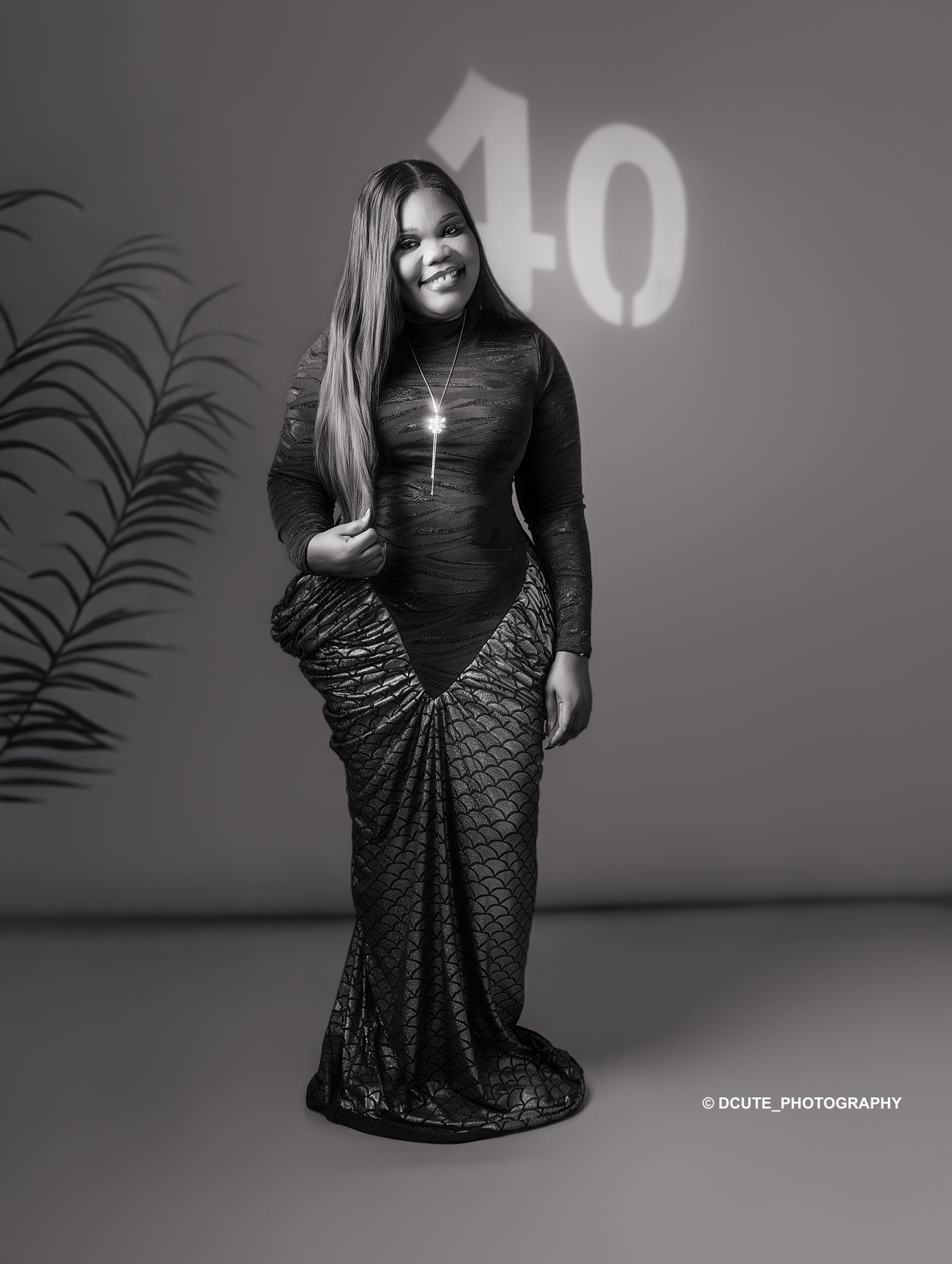 Black and white portrait of a woman in an elegant mermaid gown posing in front of a number 40 backdrop.