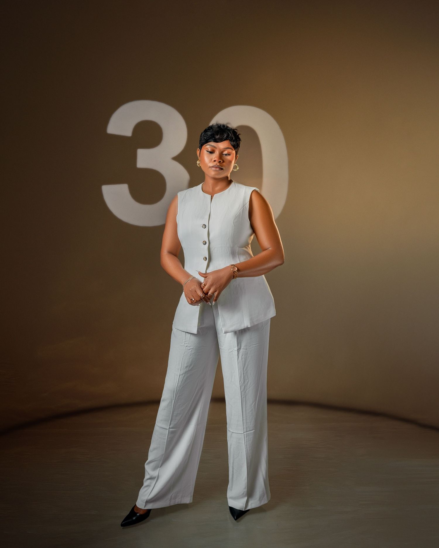 Stylish woman in white wide-leg pantsuit stands confidently in front of large number 30 backdrop in toronto birthday photography