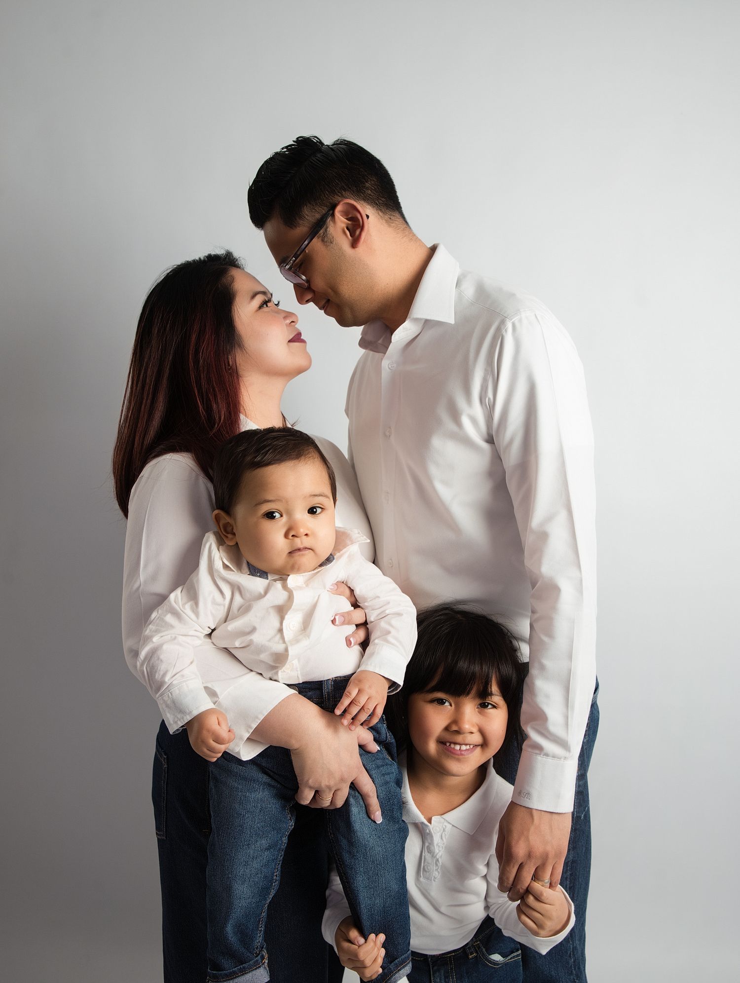 Asian family of four in matching white shirts and jeans share a tender moment in studio Family portrait photographer Downtown Toronto