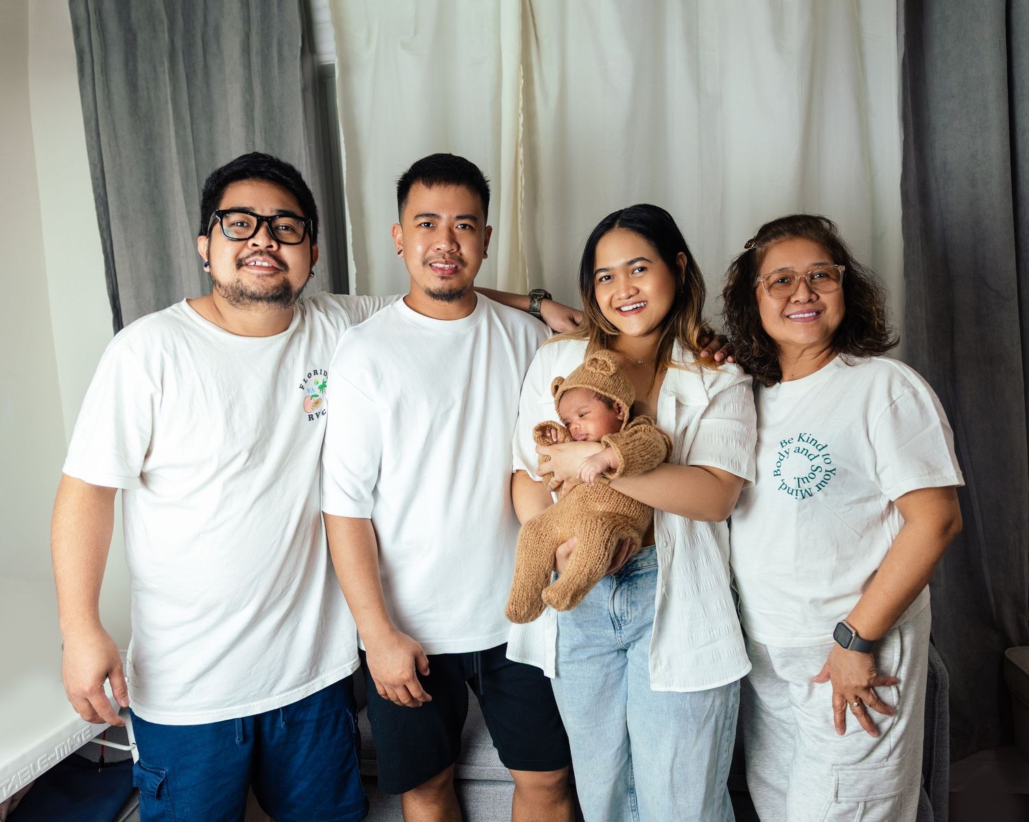 Happy family of five in matching white shirts posing with newborn baby in bear outfit by a Newborn photographer in Toronto home session
