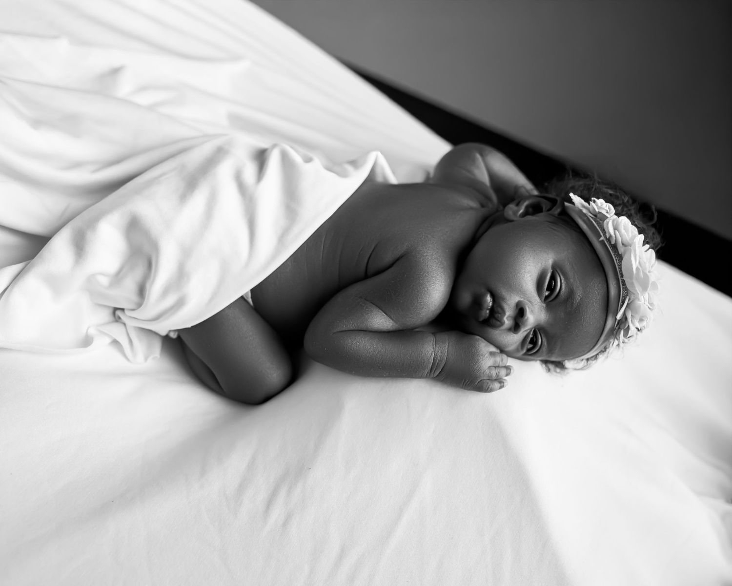 Black and white photo of a peaceful newborn baby girl wearing a floral headband, IN A WEST TORONTO PHOTOGRAPHER PORTFOLIO