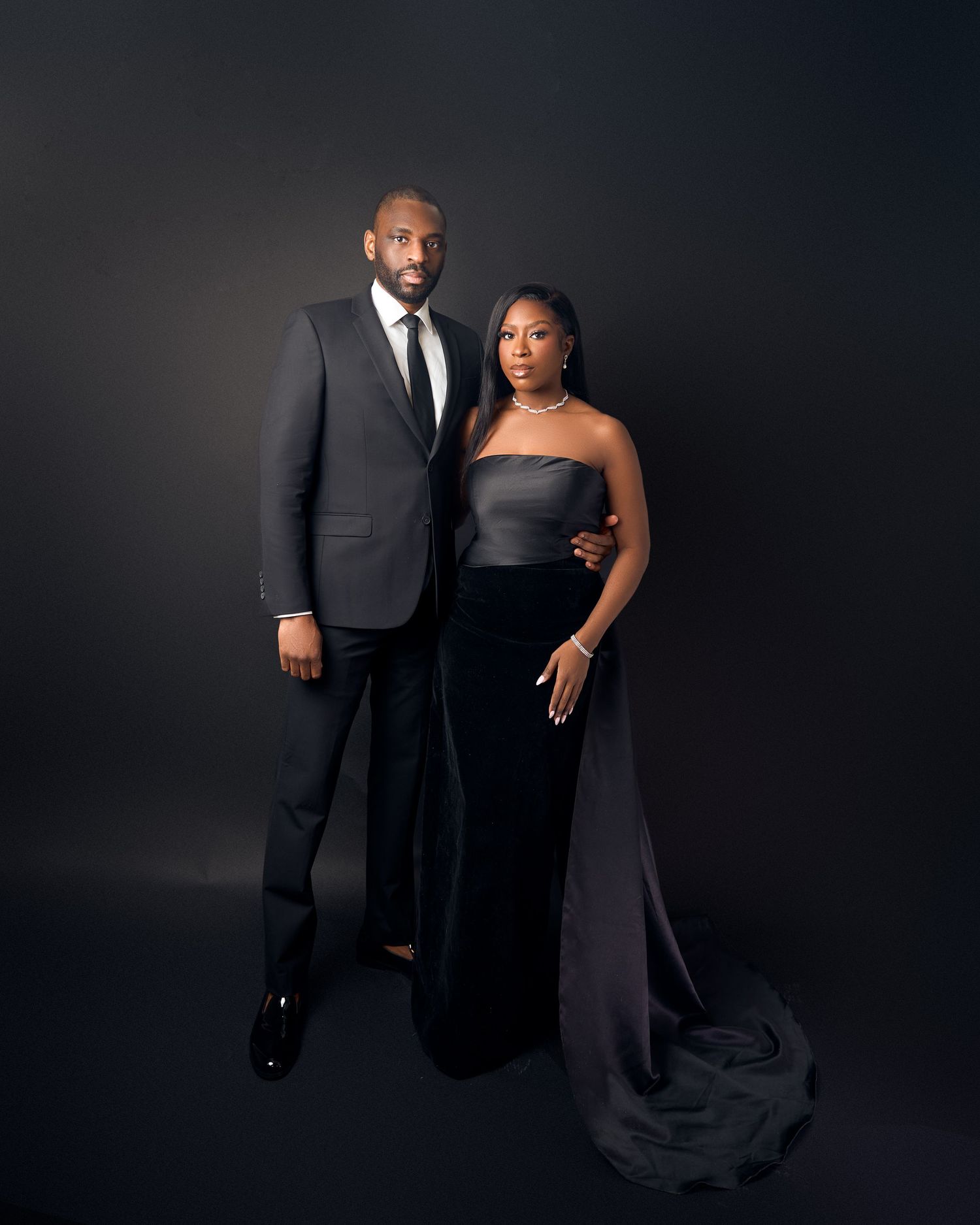 Elegant couple in matching black formal attire posing together against a dark studio photshoot for birthday in toronto