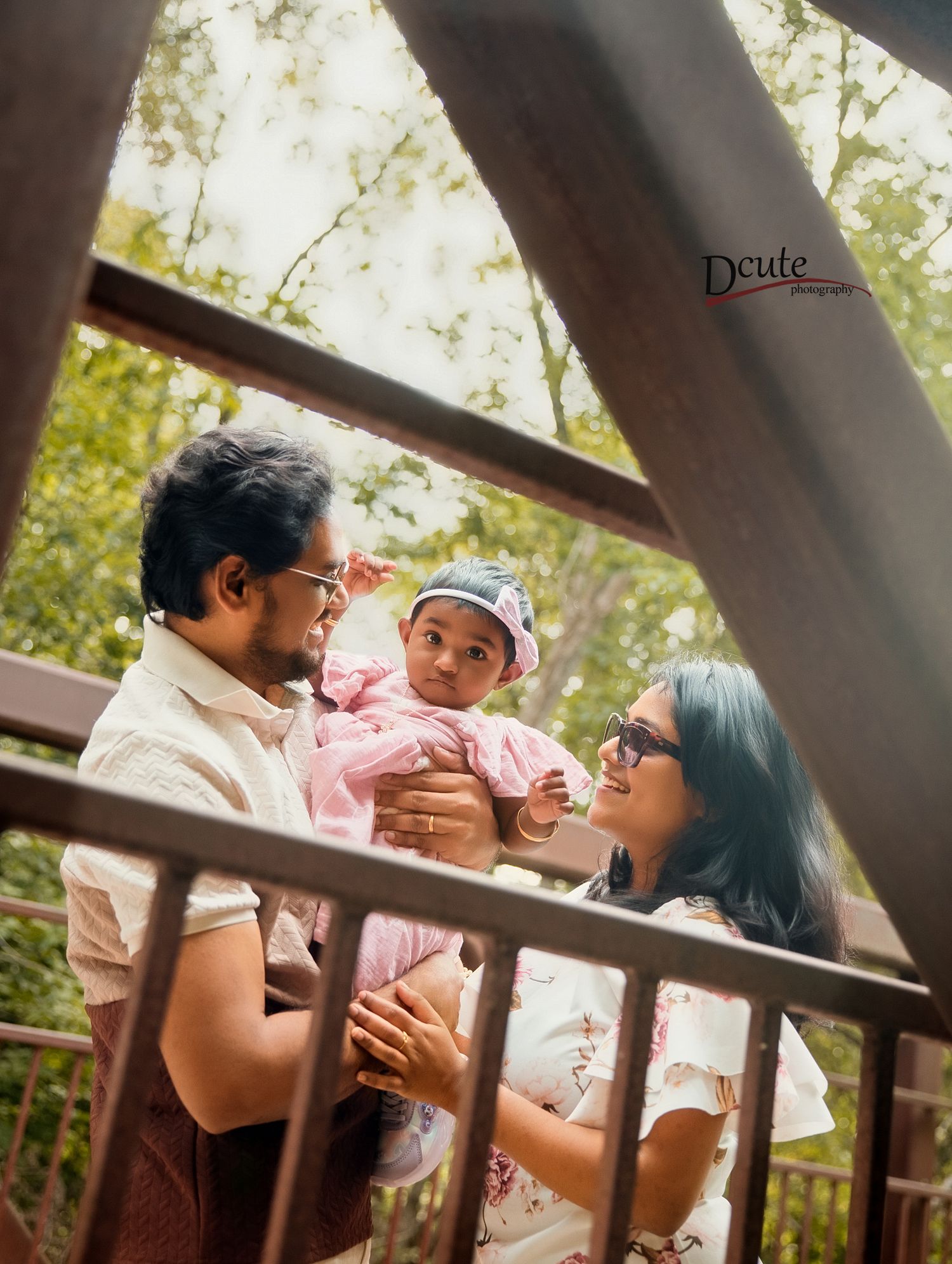 Young couple sharing a tender moment with their newborn baby on a wooden bridge surrounded by trees.