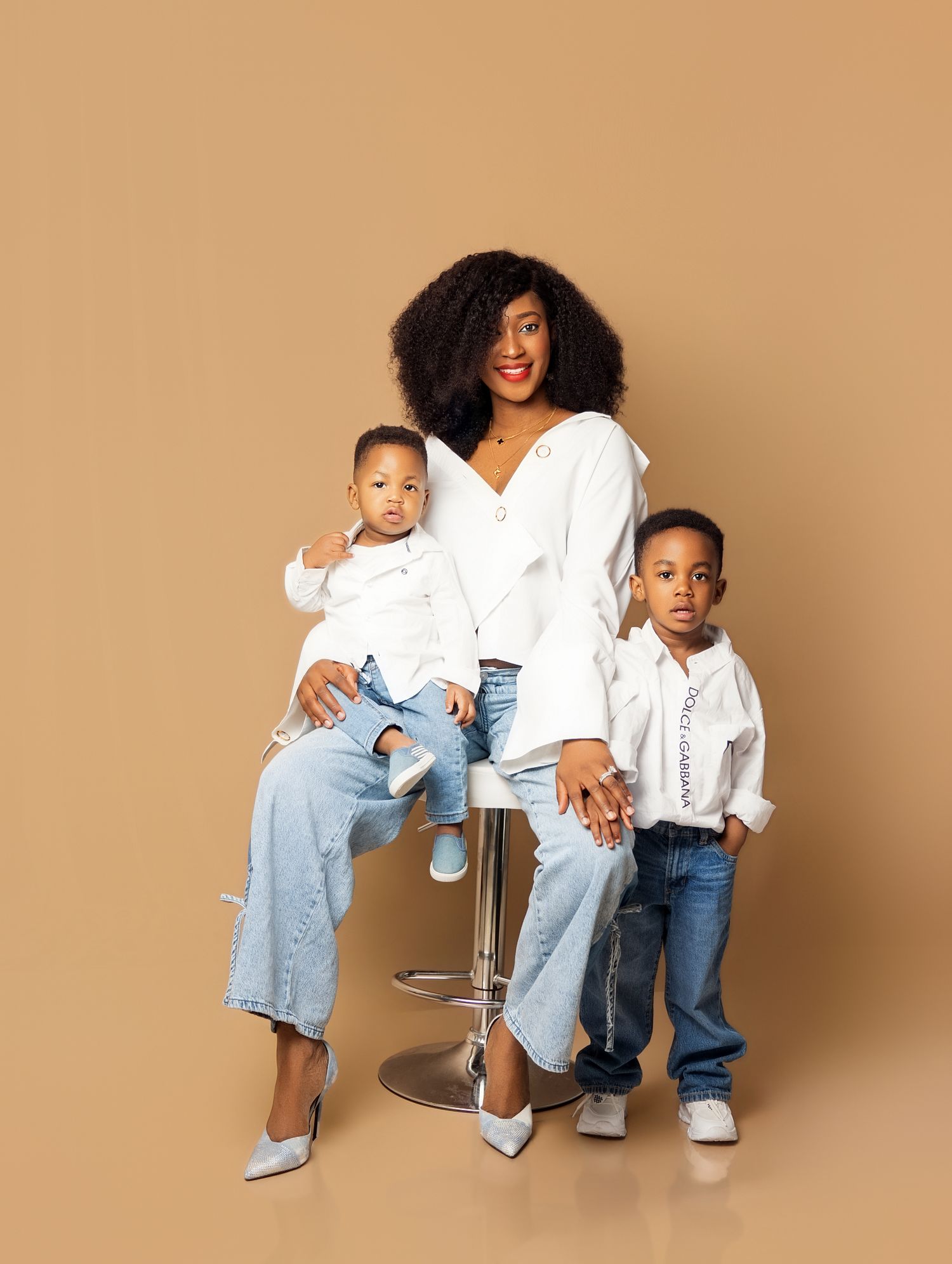 A woman in top and jeans sits on a stool with two young children in matching white shirts and jeans. captured by Toronto family photogher