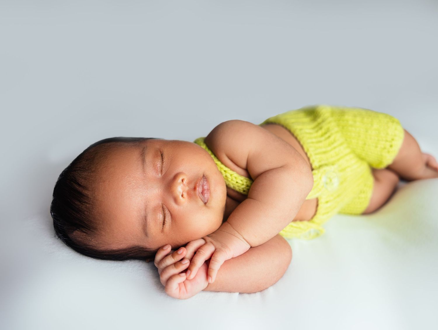 Peaceful newborn baby in yellow knit outfit sleeping on white background.