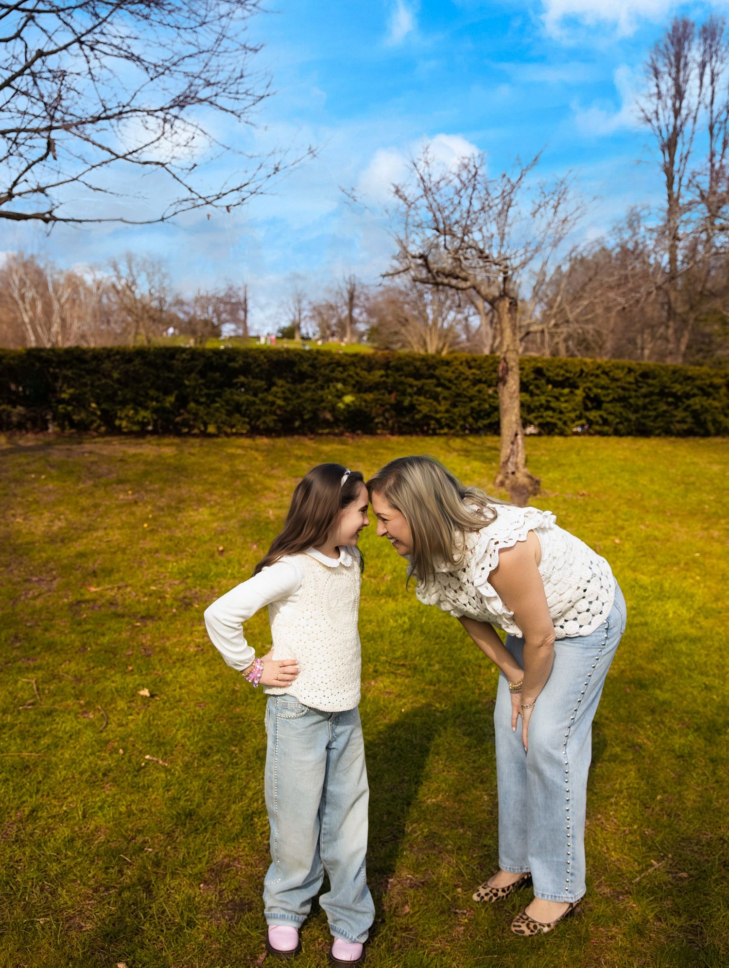 Family photos with toddlers Toronto, parents cA woman bends down to touch foreheads with a young girl in a sunny green park with blue skies.