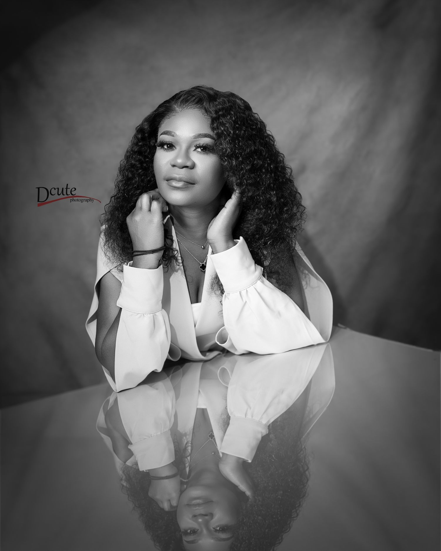 Black and white studio portrait of young woman leaning on reflective surface she looking at birthday photography packages toronto