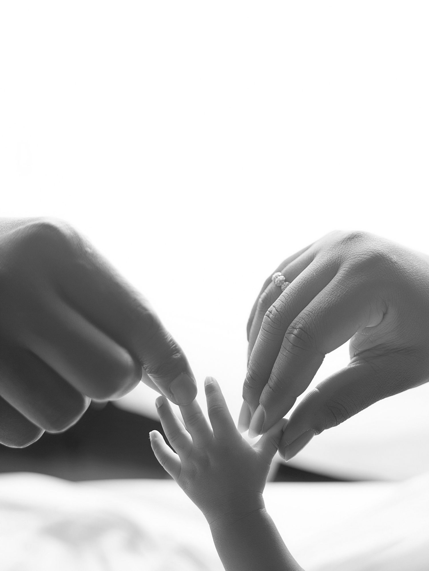 Black and white photo of adult hands gently touching a newborn baby's tiny hand, symbolizing love and new life.