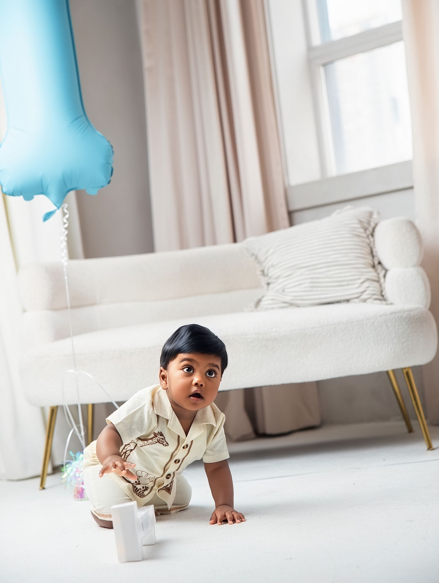 Curious toddler crawls on floor near a blue number one balloon during first birthday photoshoot in North york