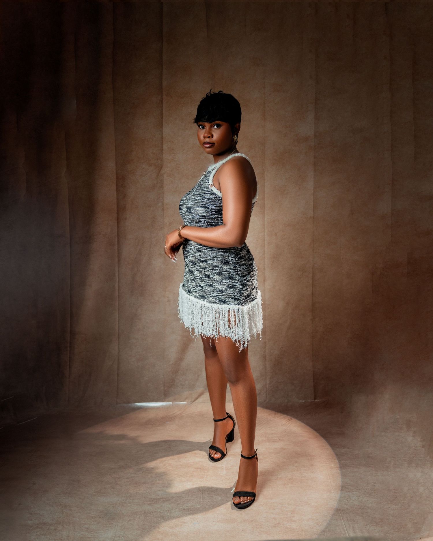 Woman in sparkly fringe mini dress poses elegantly in spotlight against textured brown backdrop in toronto birthday photography