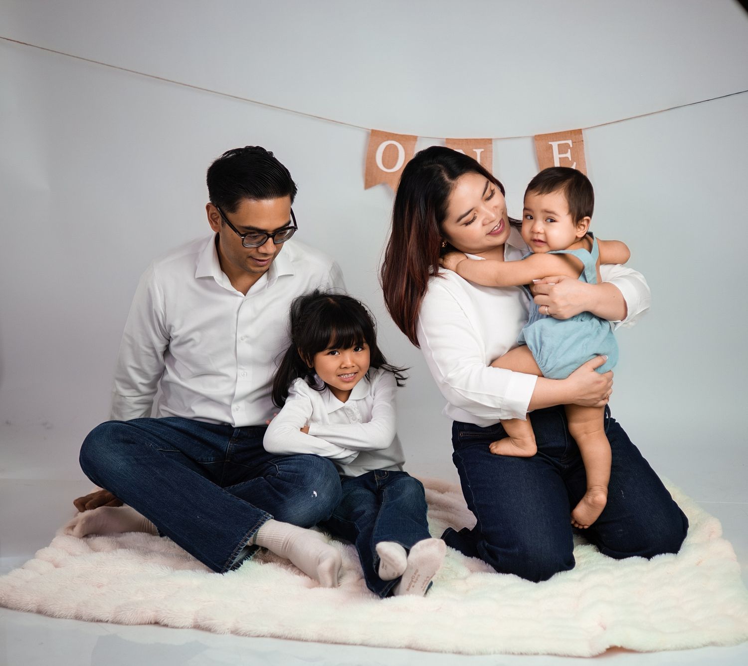 Asian family of four in white and denim sit casually on a rug beneath a ONE banner in a Family photography near Downtown Toronto